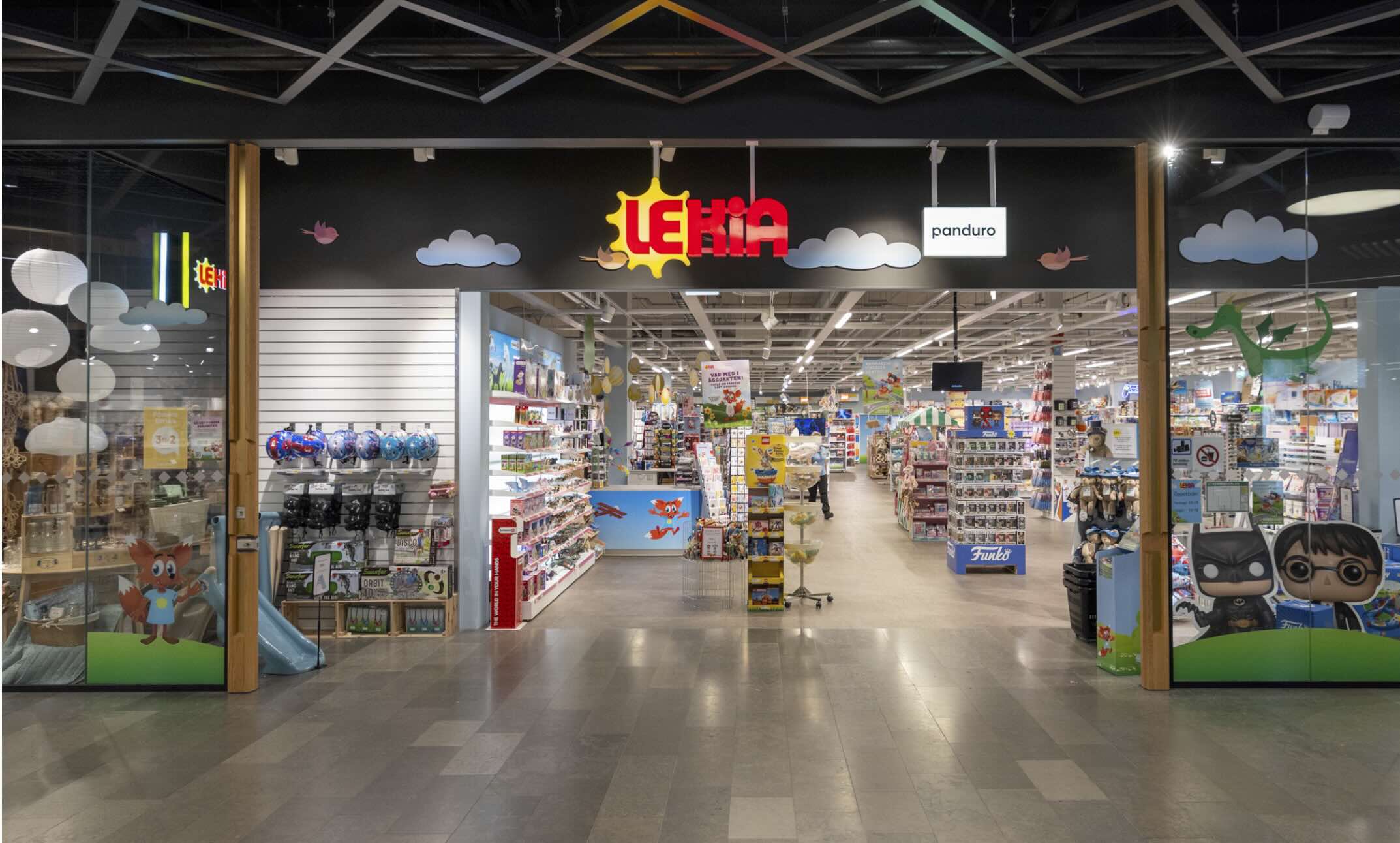En leksaksbutik med texten LEKIA i gult och rött och texten panduro bredvid öppnar mot en galleria; inuti står färgglada hyllor och varor.