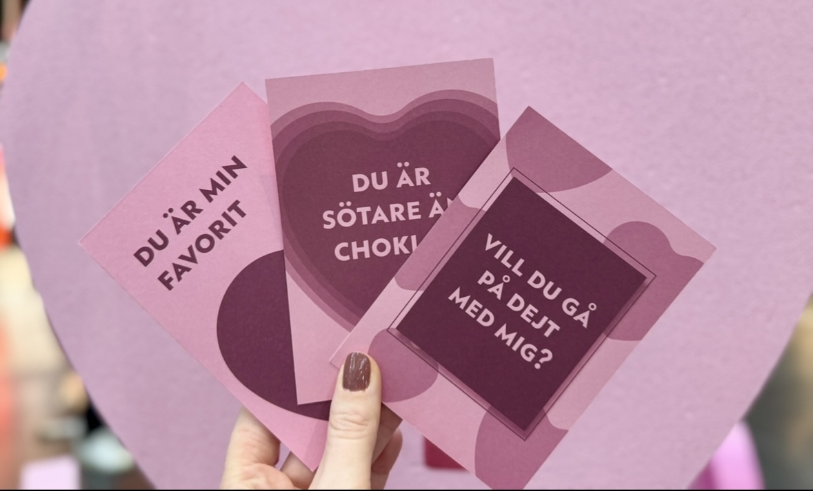 Tre rosa kort med alla hjärtans dag hälsningar hålls upp av en hand.