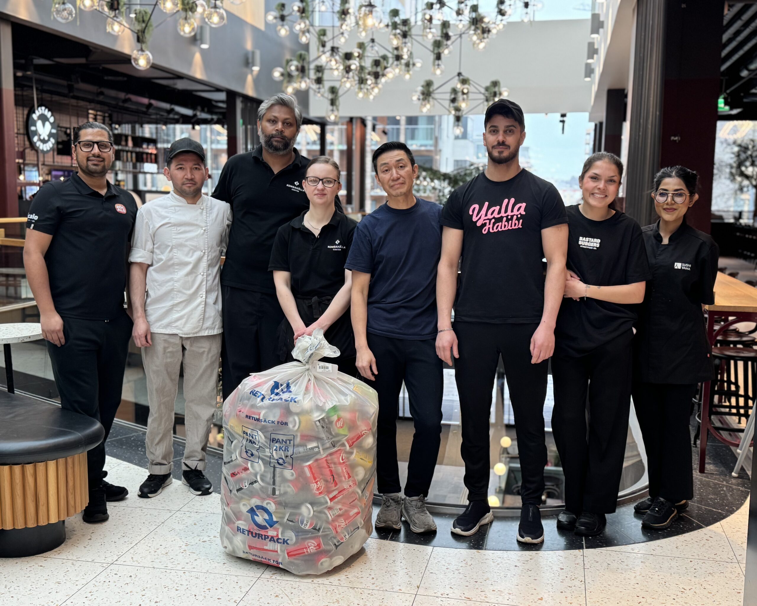 En grupp personer från Food Hall står framför en stor kasse med pant