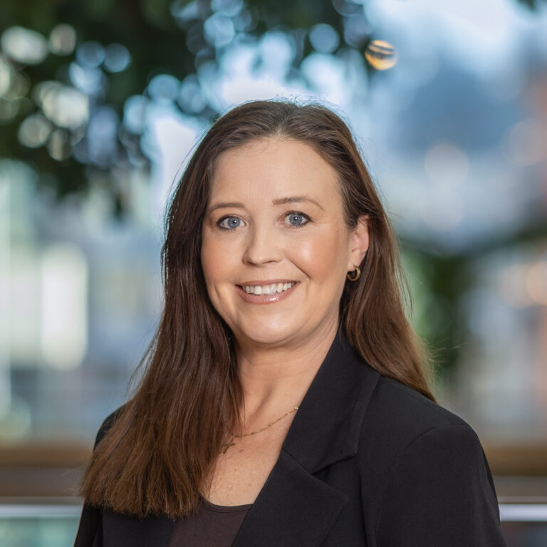 Kvinna med brunt hår, blår ögon och svart kavaj