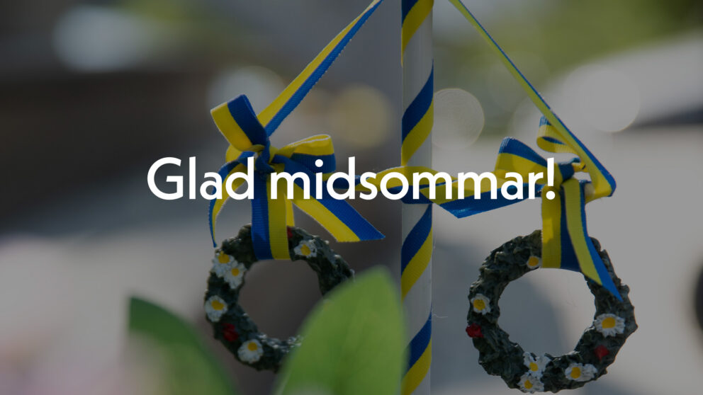 En midsommarstång i trä med texten Glad midsommar! i vitt