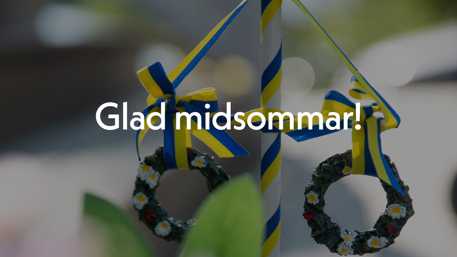 En midsommarstång i trä med texten Glad midsommar! i vitt