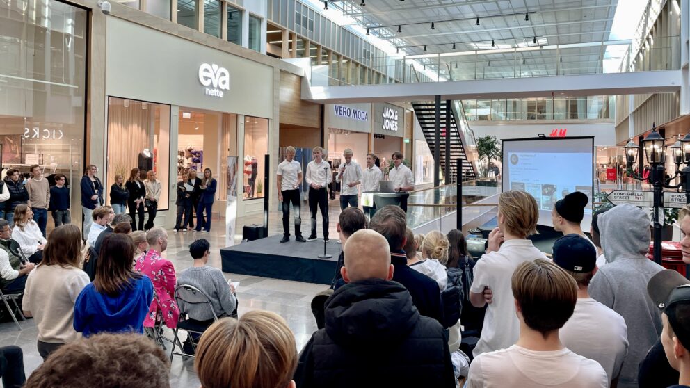 Fem killar står på en scen med mycket åhörare framför sig